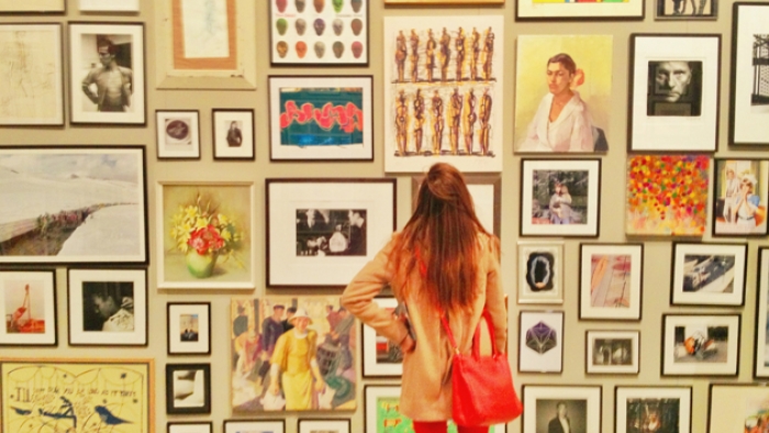 A woman stands looking at a wall covered with framed pieces of art.
