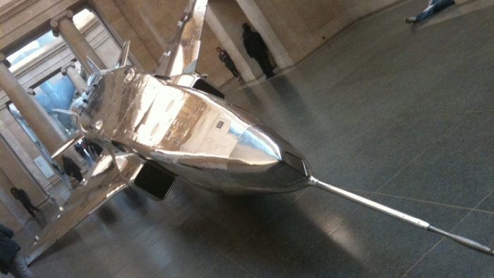 A shiny metal model of an aircraft in a big building.