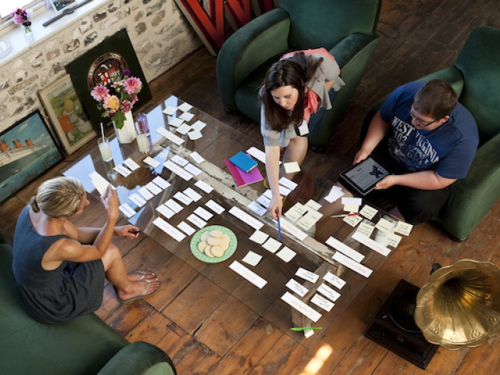 Three people sit at a glass coffee table sorting cards for a web design project.