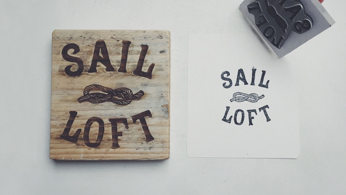 The Sail Loft word mark lasered onto wood and stamped onto a piece of paper.