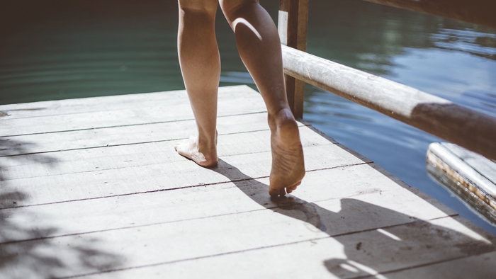 Bare feet walking on a wooden pontoon over a lake.
