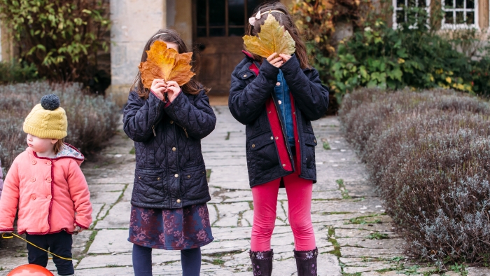 Three children standing outside an LFH hotel, two holding leaves over their faces.