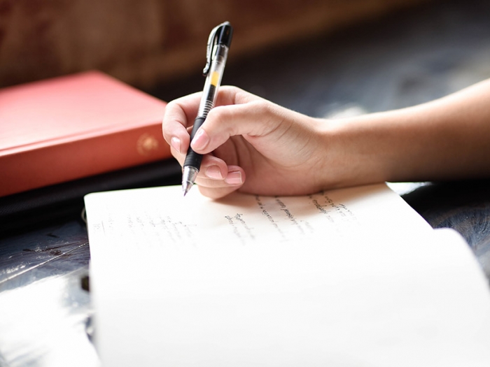 A hand holding a pen poised above a notebook.