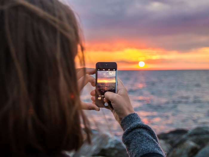 A woman takes a photo of the sunset on her iPhone.