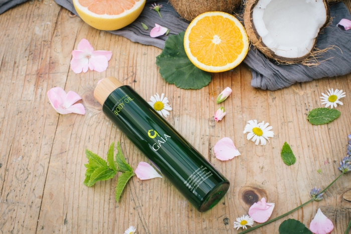 A bottle of Gaia body oil surrounded by oranges, coconuts and mint.