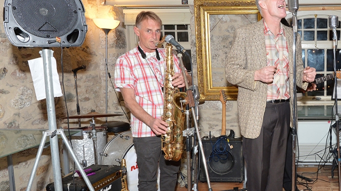 One man plays a saxophone while another sings.